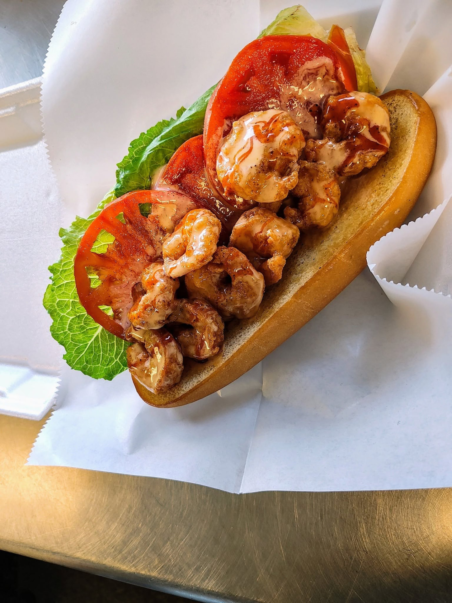 Crispy shrimp roll drizzled with sauce on a toasted bun