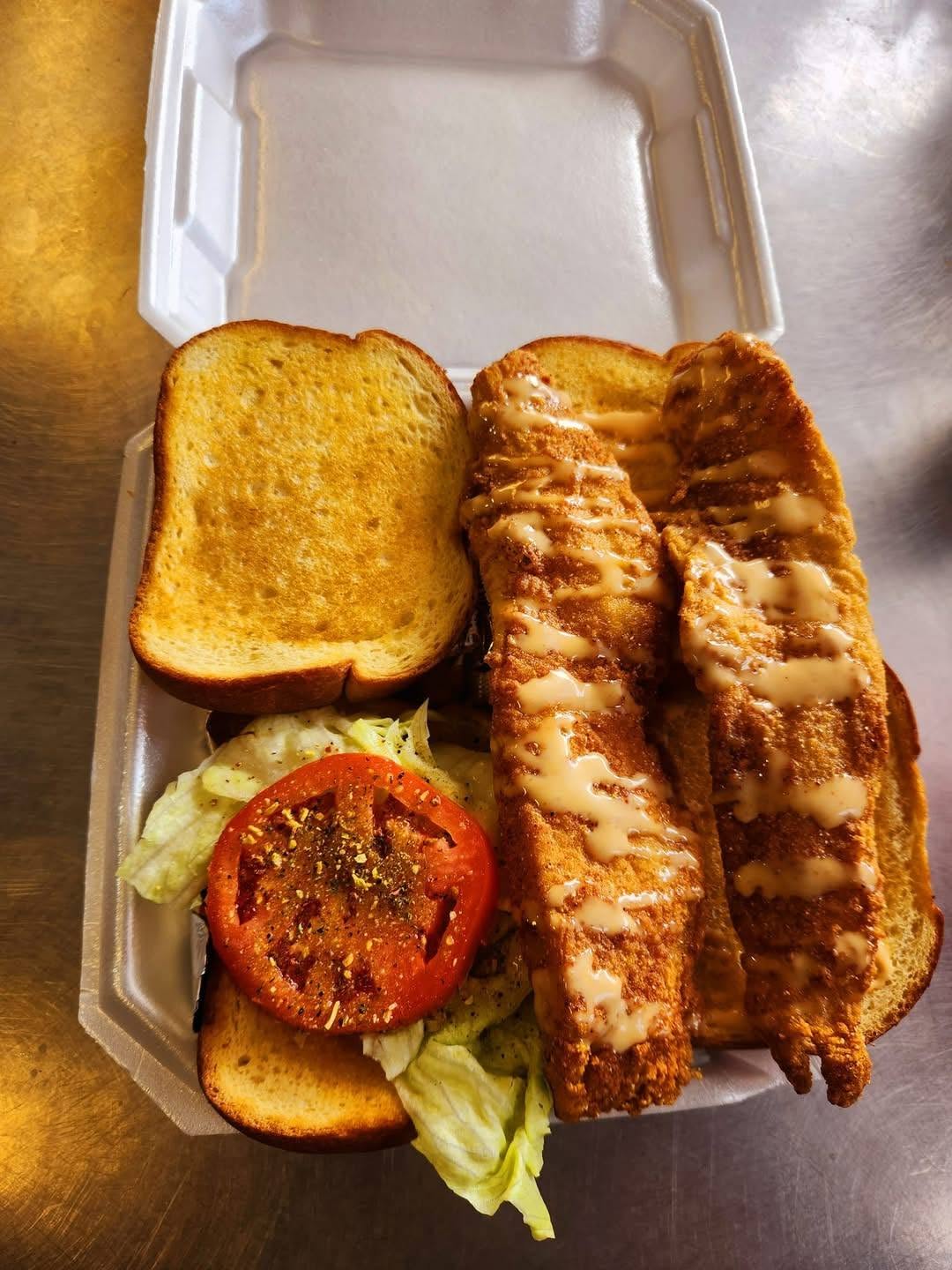 Two fried fish fillets drizzled with sauce on Texas toast with lettuce and tomato