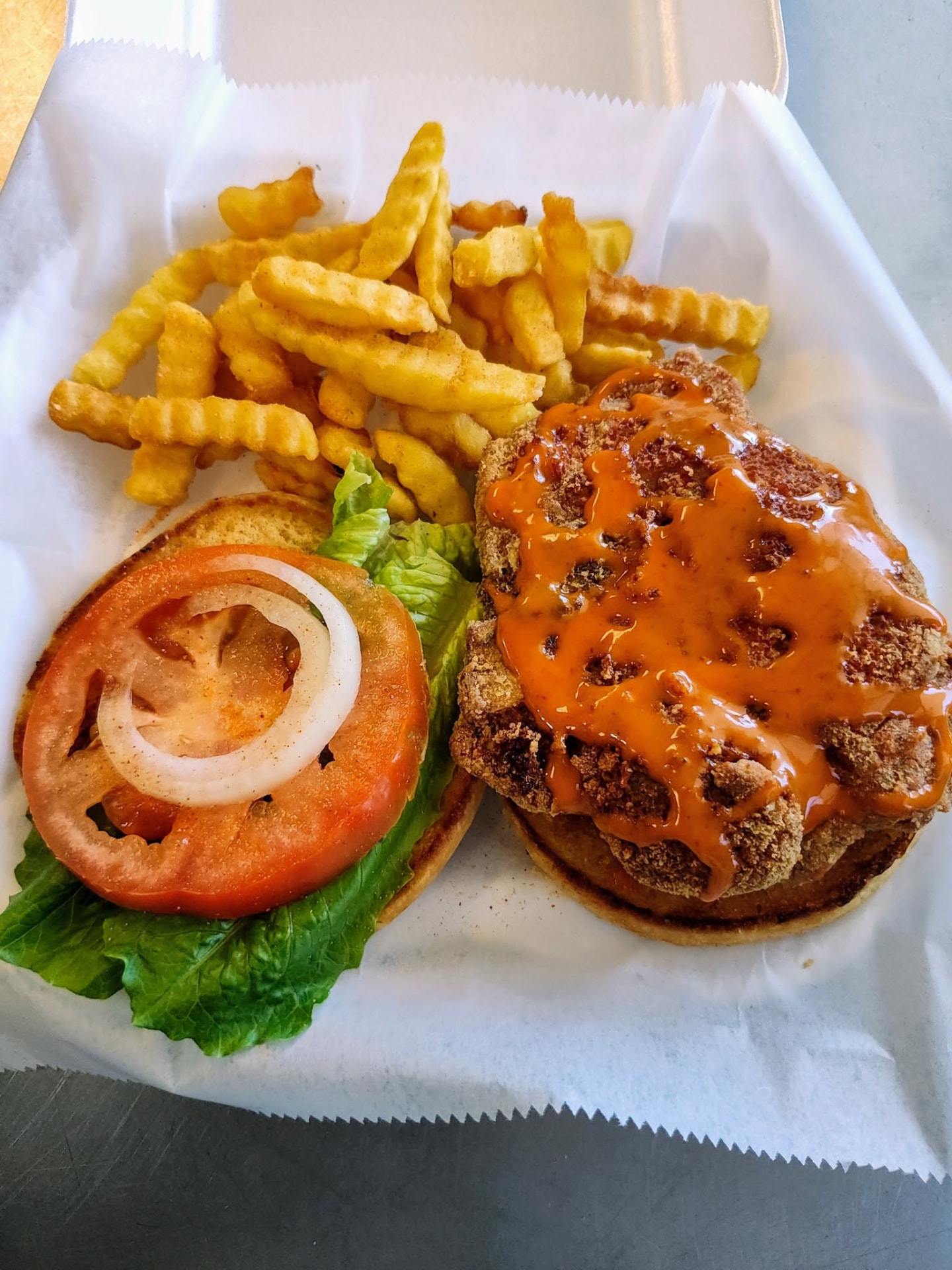 Fried fish sandwich topped with sauce, served open faced with fries